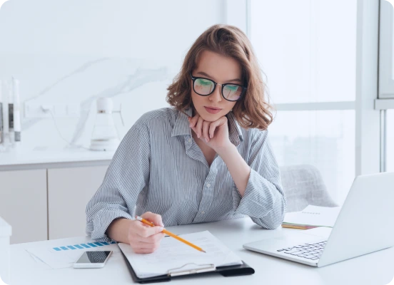 A person in a striped shirt sits at a desk with a laptop, notebooks, and a phone, writing notes and reviewing Agents for Landlord.